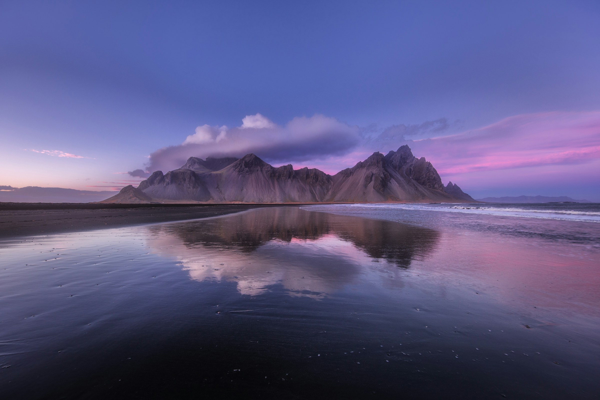 The Vestrahorn mountain range reflected in wet black sand on the Icelandic coast