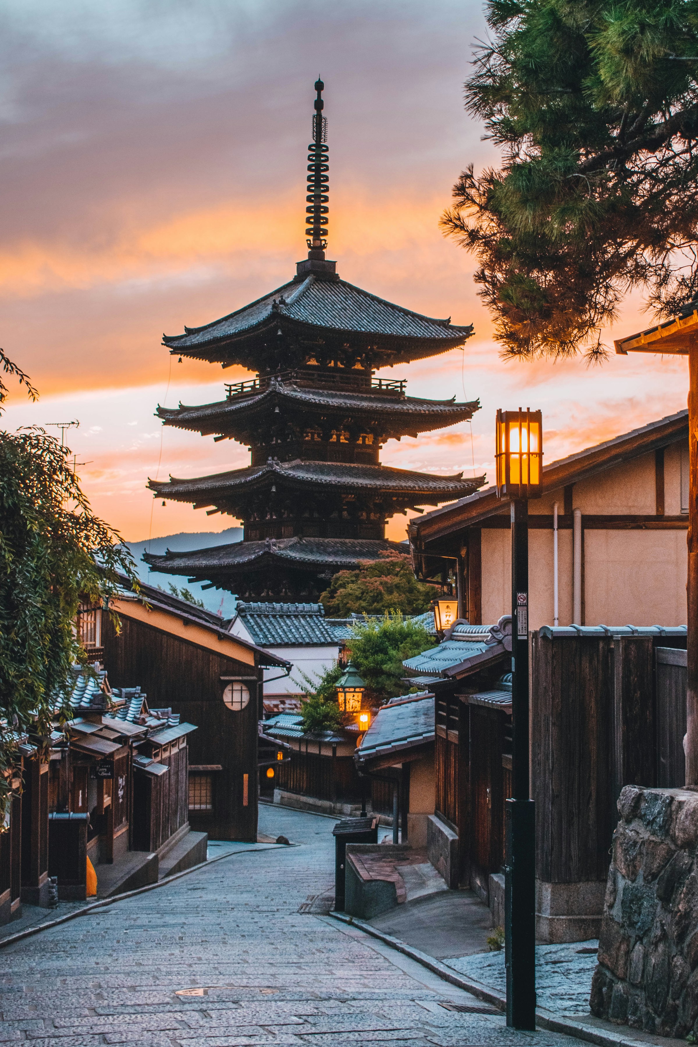 A wooden pagoda rising above a narrow street of low tiled roofs in Kyoto at golden hour