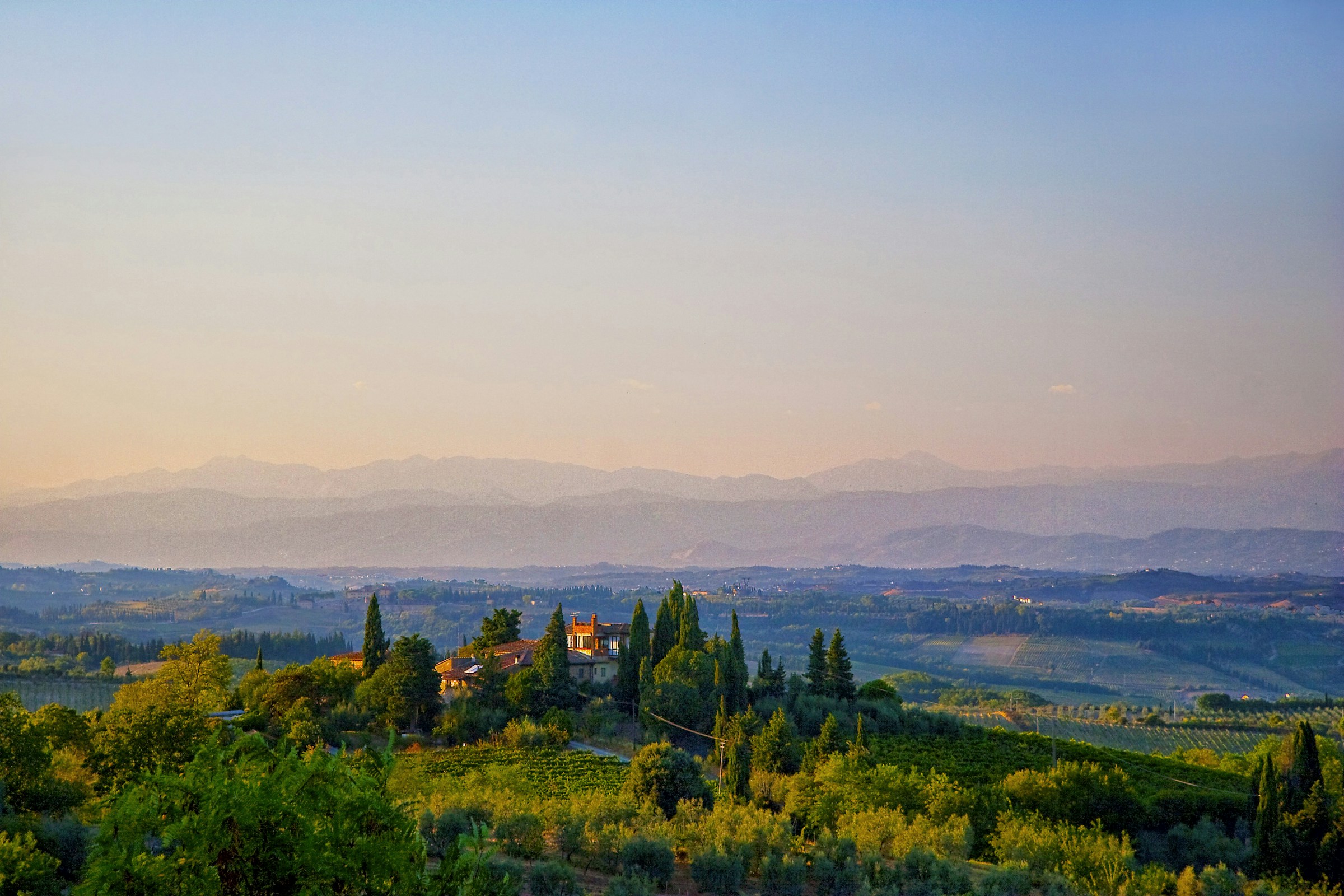 A stone villa ringed by cypress trees on a hill above a Tuscan valley